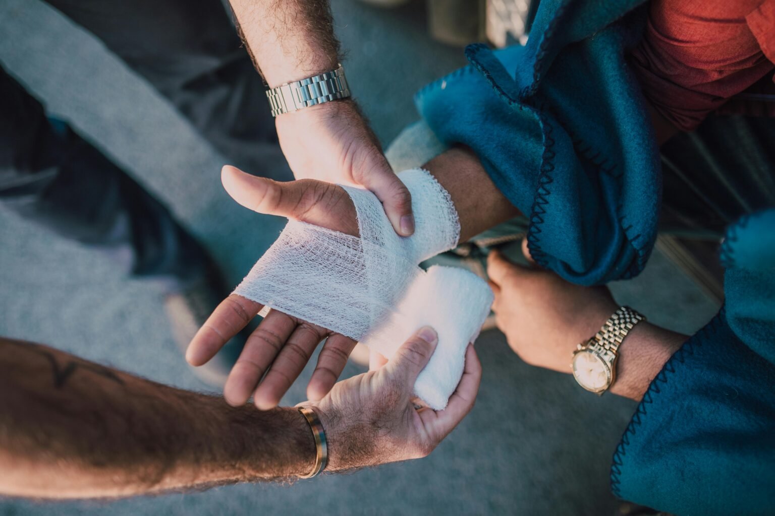 Workplace First Aid Training 1 Close-up of two people bandaging an injured hand outdoors, focusing on first aid care.