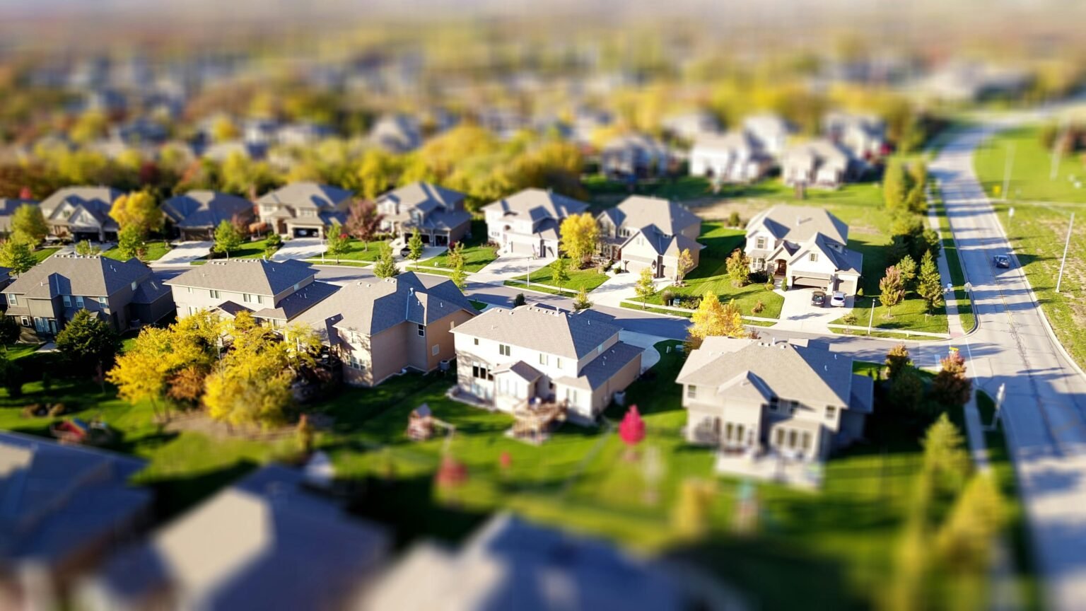 Property Management Training Certificate 1 Tilt-shift aerial photo of a suburban neighborhood with green lawns and roads.