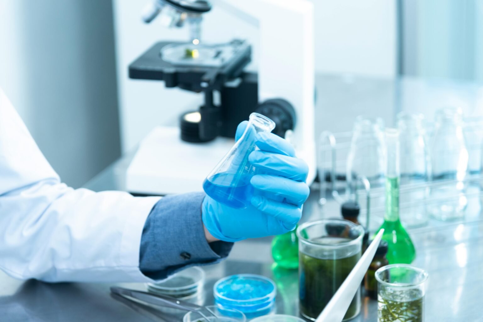 Chemical Plant Processing Safety and Management 1 Scientist in gloves analyzing blue liquid in a laboratory setting with microscope and glassware.