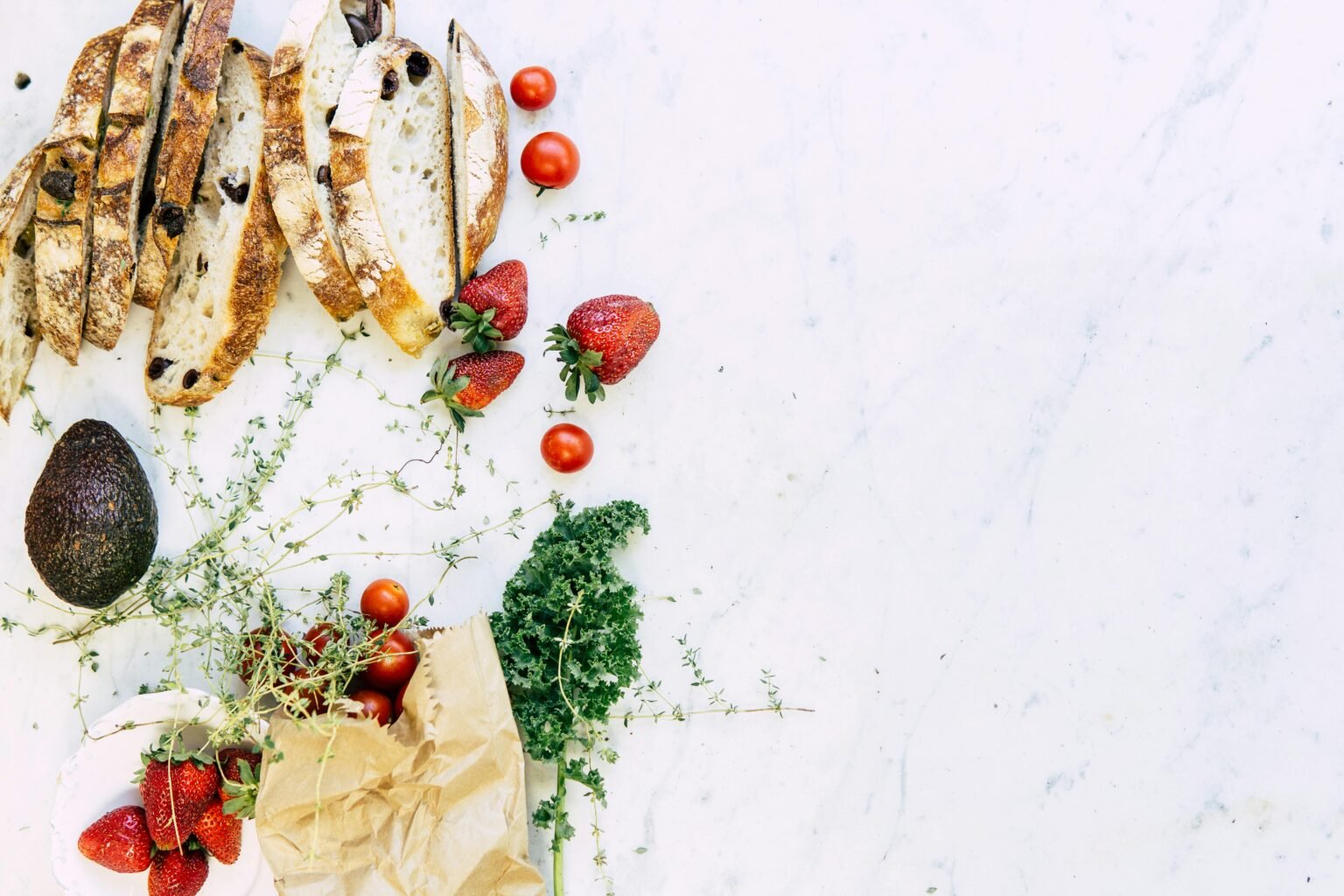 A flat lay of fresh ingredients including bread, strawberries, and avocado on marble. Perfect for food and lifestyle imagery.